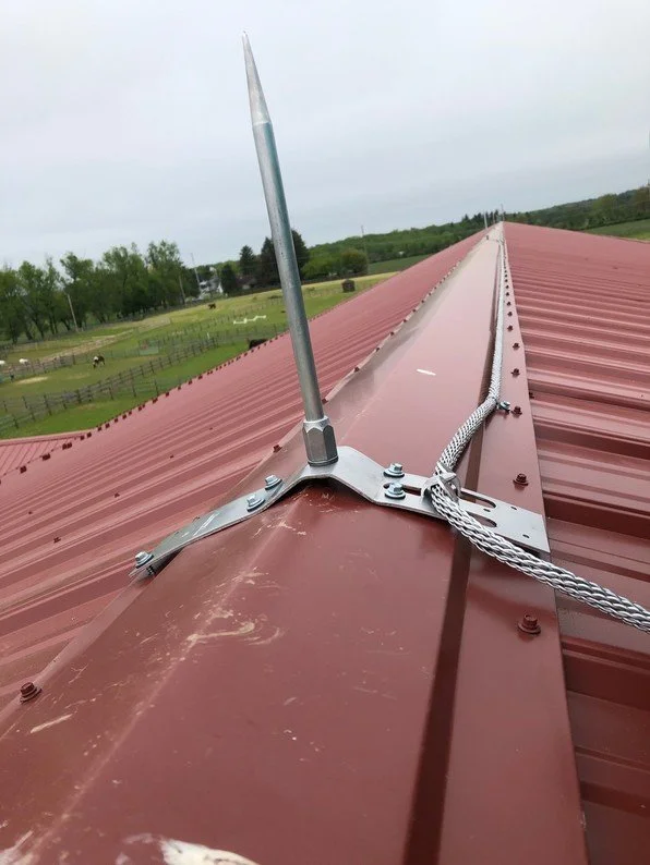 Close-up reference of an air terminal, bracket, and braided conductor on a standing seam metal roof.